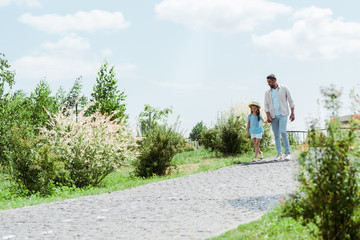 handsome father and daughter walking near green plants and holding hands