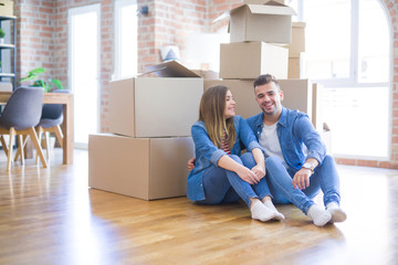 Young beautiful couple in love moving to new home, sitting on the floor very happy and cheerful for new apartment around cardboard boxes