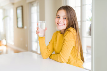 Beautiful young girl kid drinking a fresh glass of water with a happy face standing and smiling...
