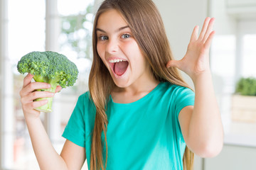 Beautiful young girl eating fresh broccoli very happy and excited, winner expression celebrating...