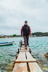 Fototapeta premium man walking by small wooden pier overcast weather stormed sea on background
