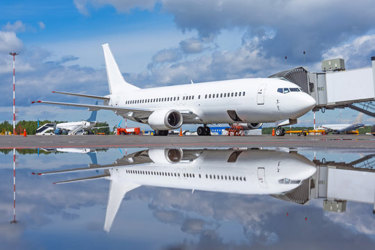 Passenger aircraft parked through the ladder gangway at the terminal, flight service, view in mirror image in a pool of water after rain.
