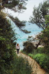 Fototapeta premium woman in raincoat walking to the sea by trail between trees