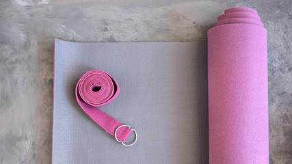 Yoga mat  with yoga  strap on cement floor. Yogi essentials for any type of practice. Top view, copy space.