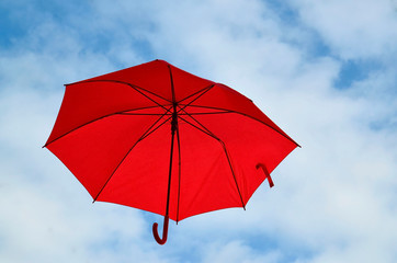 Red umbrella floating in the air on a blue cloudy sky background with space for text.