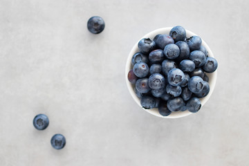 Fresh blueberries in a white bowl on a gray background. Top view.