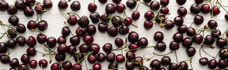 panoramic shot of fresh, sweet, red and ripe cherries with droplets on wooden table