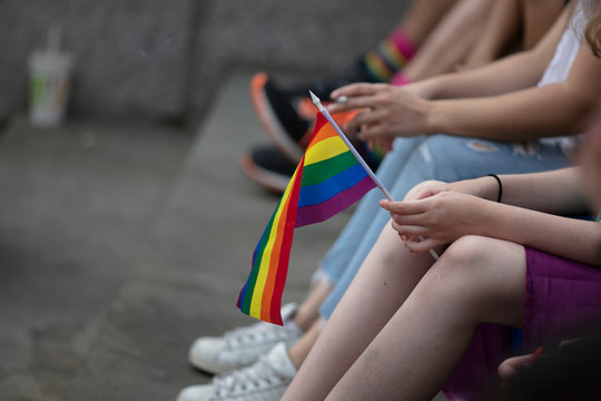 A young person holding a gay pride flag whilst sitting down