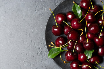 Lots of ripe cherries on a black plate. Dark background. Flat lay, copy space