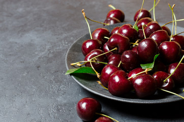 Lots of ripe cherries on a black plate. Dark background, copy space