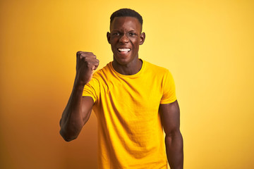 Fototapeta na wymiar Young african american man wearing casual t-shirt standing over isolated yellow background angry and mad raising fist frustrated and furious while shouting with anger. Rage and aggressive concept.