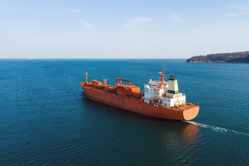 Fototapeta premium Aerial view of sea vessel for transportation of a cargo vessel at high speed is drifting near the seaport of the city at sunset. Ship on the background of blue sea water. Import, export 