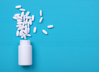 Pills and white bottle on blue background.
