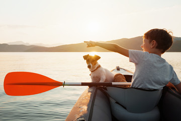 Happy boy with his dog Jack Russell Terrier paddling an inflatable kayak on the water mountain lake...