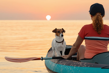 Red-haired young woman is rowing on an inflatable kayak by the sea with a dog Jack Russell Terrier...