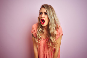 Young beautiful woman wearing t-shirt standing over pink isolated background angry and mad screaming frustrated and furious, shouting with anger. Rage and aggressive concept.