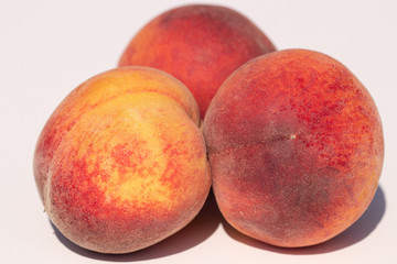 Three juicy peaches on a white background in sunlight