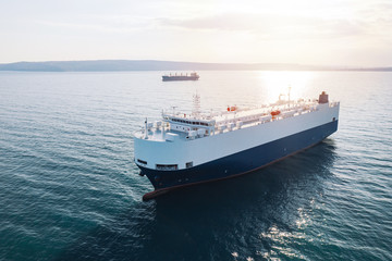 Fototapeta na wymiar Aerial view of high-speed sea vessel for transportation of cargo vessel at high speed is drifting near the seaport of the city at sunset. Ship on the background of blue sea water. Import, export. Top