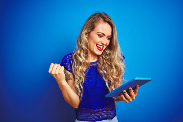 Young beautiful woman using tablet over blue isolated background screaming proud and celebrating victory and success very excited, cheering emotion