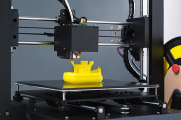 Printing on 3D printer figurines toys ship from yellow plastic close-up. Clear movements of the...
