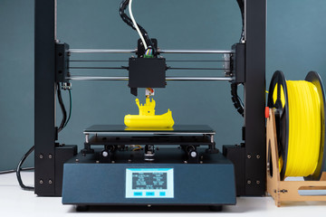 Printing on 3D printer figurines toys ship from yellow plastic close-up. Clear movements of the...