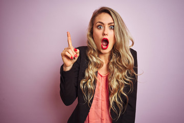 Obraz premium Young beautiful business woman wearing elegant jacket standing over pink isolated background pointing finger up with successful idea. Exited and happy. Number one.