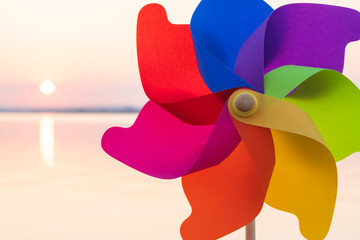 A round colored plastic pinwheel with a blowing wind stands on the sand by the sea against the smooth surface of the sea and a bright pink sunset. Toy mill on the sea beach. Large disk sun. Copyspace