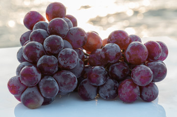 Cluster of fresh and juicy purple grapes - On a table and lights reflected by the waves of the sea decorating the photo