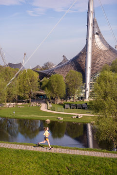 Olympia Park, Munich, Bavaria, Germany: A young female runner running at the "Olympia Berg" (hill) in the Olympiapark with a view over the lake and city.