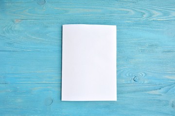 Blank sheet of white paper for design banner or card on textured blue background, selective focus. Clear page with empty space for image or text on wooden turquoise backdrop. Mockup concept 