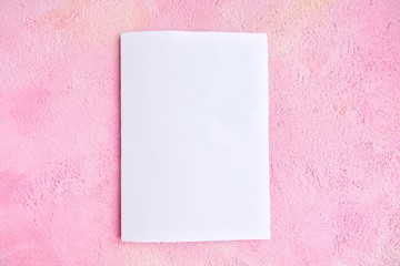 Blank sheet of white paper for design banner or card on textured pink background, selective focus. Clear page with empty space for image or text on pink plaster backdrop. Mockup concept 