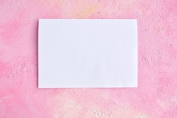 Blank sheet of white paper for design banner or card on textured pink background, selective focus. Clear page with empty space for image or text on pink plaster backdrop. Mockup concept 