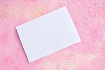 Blank sheet of white paper for design banner or card on textured pink background, selective focus. Clear page with empty space for image or text on pink plaster backdrop. Mockup concept 