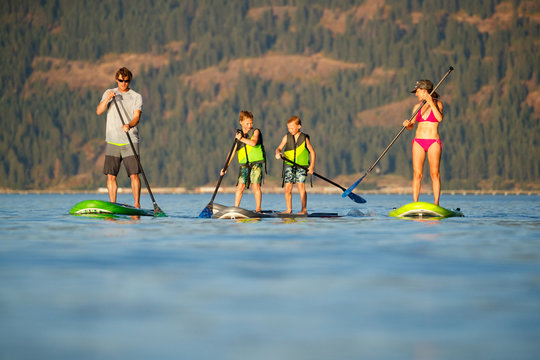 A young family stand up paddle boards at sunset in the summer at Lake Pend Oreille in north Idaho.
