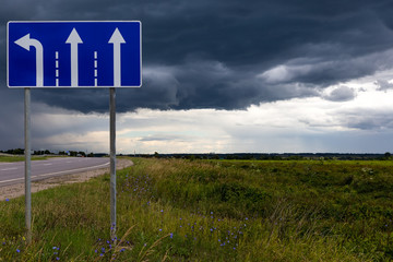 Road sign of the direction of movement against the sky with dark rain clouds. Choice of direction.