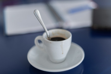 A white coffee mug on a blue table - An out-of-focus notebook and cell phone