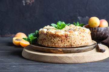 Cheesecake with apricot and crumble, fresh apricots and mint. Wooden background, rustic style. Copy space.