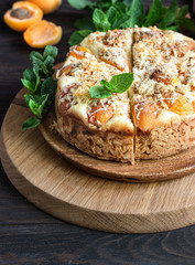 Cheesecake with apricot and crumble, fresh apricots and mint. Wooden background, rustic style. Copy space.