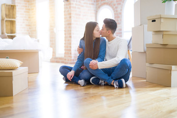 Young asian couple sitting on the floor of new house arround cardboard boxes relaxing and smiling happy