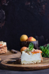 Cheesecake with apricot and crumble, fresh apricots and mint. Wooden background, rustic style. Copy space.