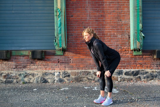 A fit, blonde female runner catches her breath near an old brick warehouse in downtown Spokane, Washington.