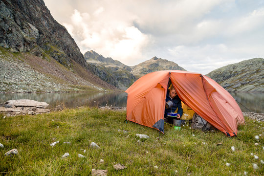 Spronser Lakes Hike, South Tyrol, Italy: A woman preparing instant food from inside her tent at the shore of the "long lake" (Langsee / Lago Lungo), one of the Spronser Lakes.