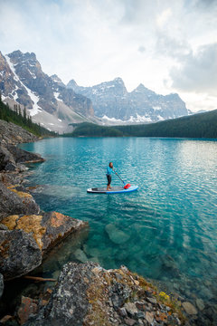 A woman stand up paddle boards at Moraine Lake in Banff National Park in Canada at dusk in the summer.