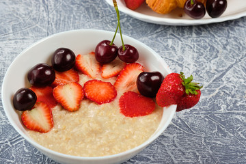 porridge in a white bowl with strawberries and cherries on a gray background