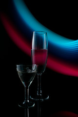 A two wine glass isolated on a black background with red, white, pink and orange neon light painting streaks of light behind them. Light wave, play of color, drawing with light.