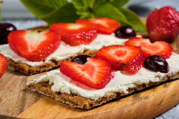 loaves with cheese, strawberries and cherries on a cutting board and gray background with mint leaves
