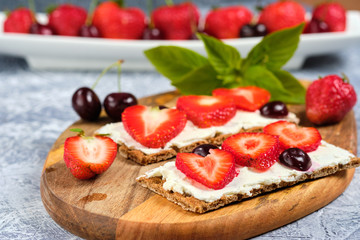 loaves with cheese, strawberries and cherries on a cutting board and gray background with mint leaves