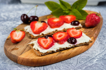 loaves with cheese, strawberries and cherries on a cutting board and gray background with mint leaves