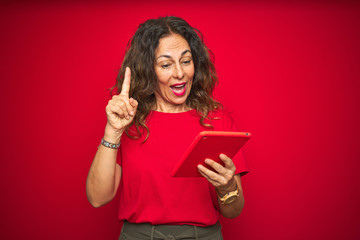 Middle age senior woman using touchpad tablet over red isolated background surprised with an idea or question pointing finger with happy face, number one