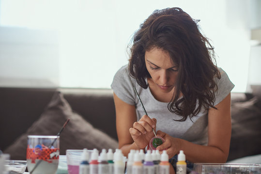 Brunette woman of latin race painting small figures with a white background.